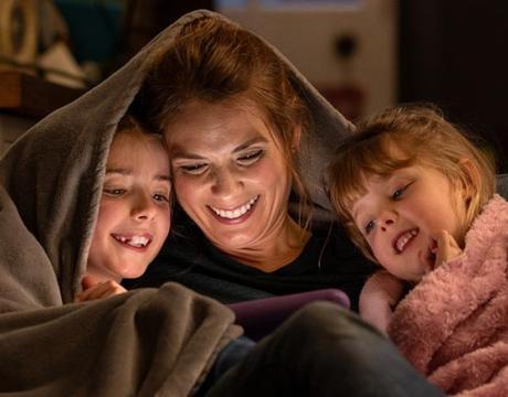 Mother and two daughters looking at device on the couch